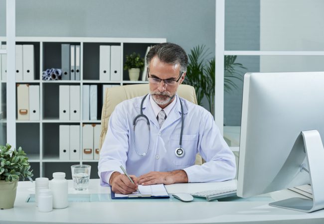 Filling medical history Middle-aged general practitioner sitting at table and filling document